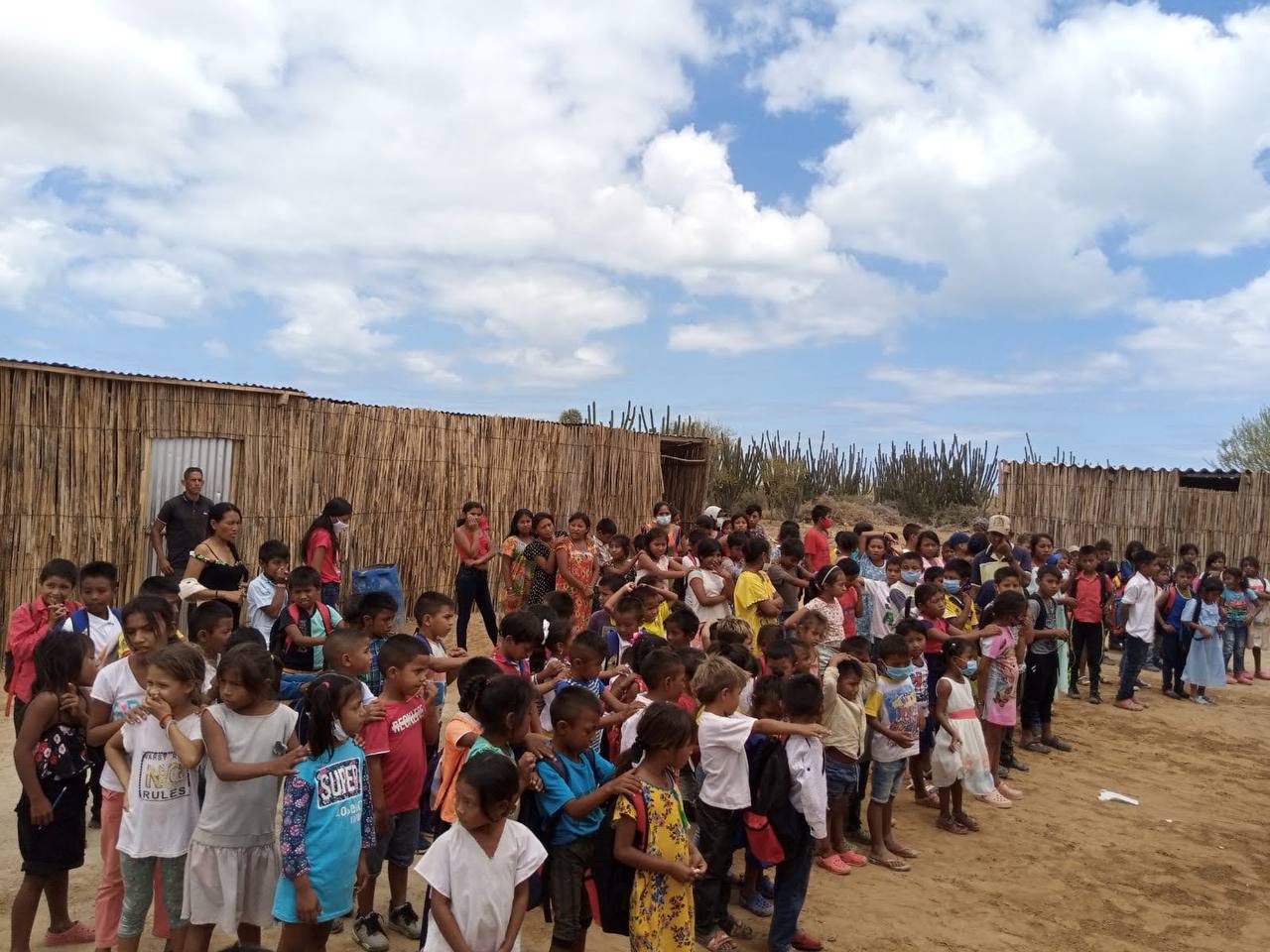 A long line of children gathered outdoors for a community day, seen from a distance.
