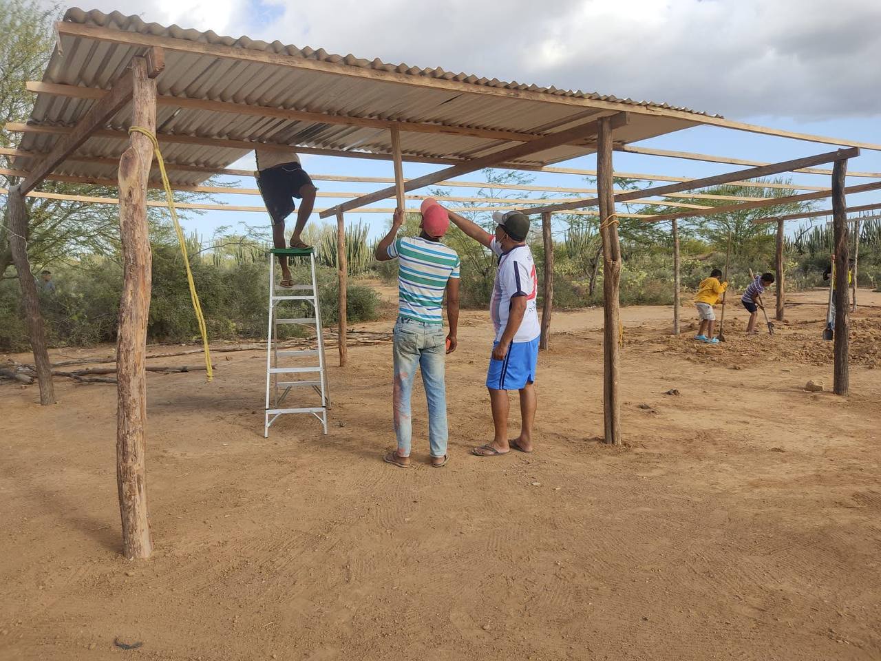 Volunteers raising the roof frame of a new community building on open ground in La Guajira, Colombia.