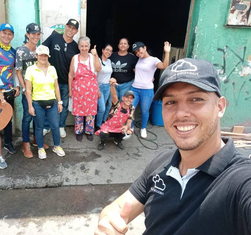 A Fundación Cloud volunteer taking a selfie with about ten other volunteers, including cooks in aprons, outside a street kitchen.